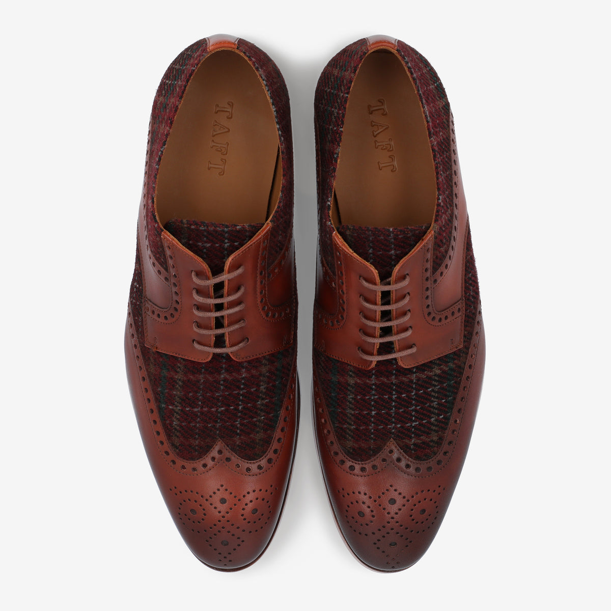 Top view of a pair of brown leather and plaid dress shoes with brogue detailing and leather soles.