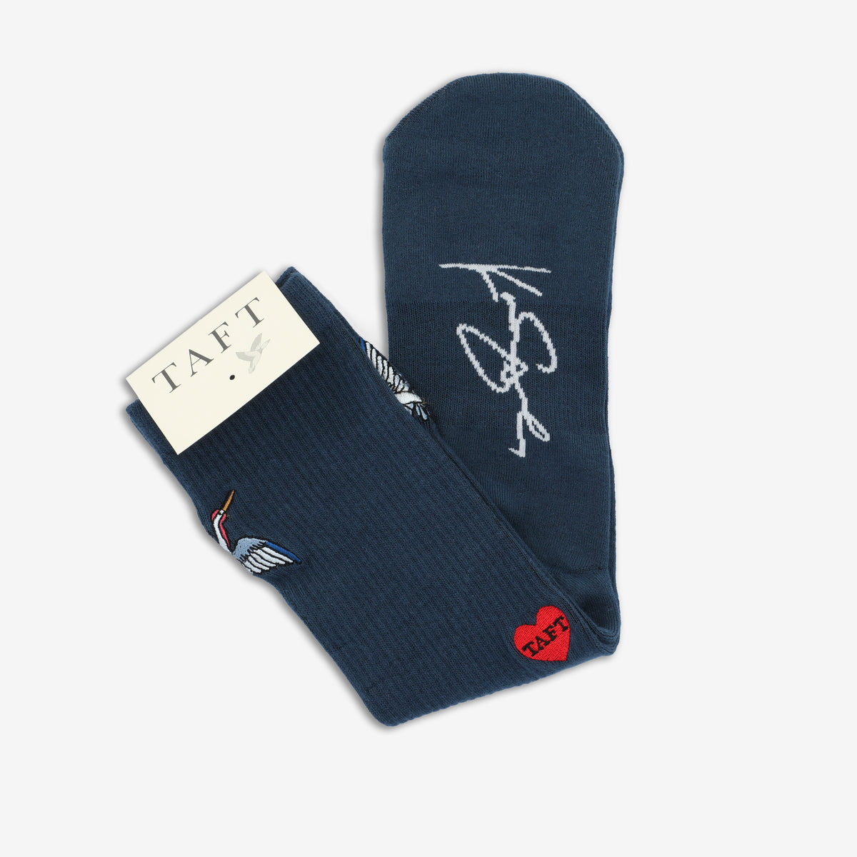 A pair of dark blue socks, one with embroidered crane and heart designs, and the other with a white signature-like print. The socks are labeled with a TAFT tag.