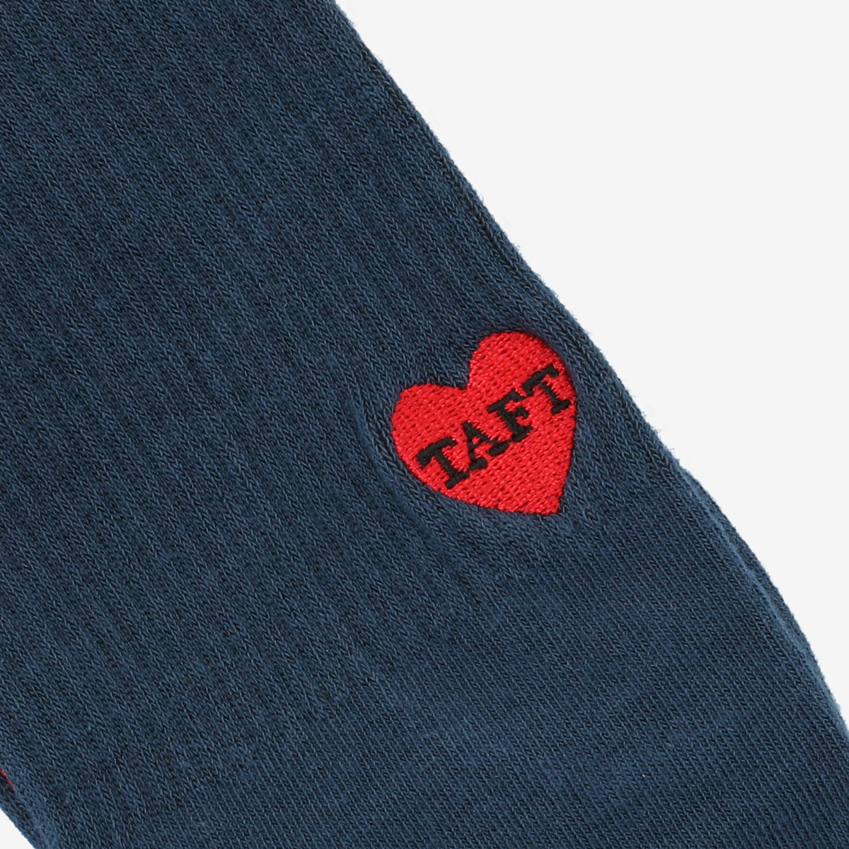 Close-up of a blue fabric with a red heart featuring the text TAFT embroidered on it.