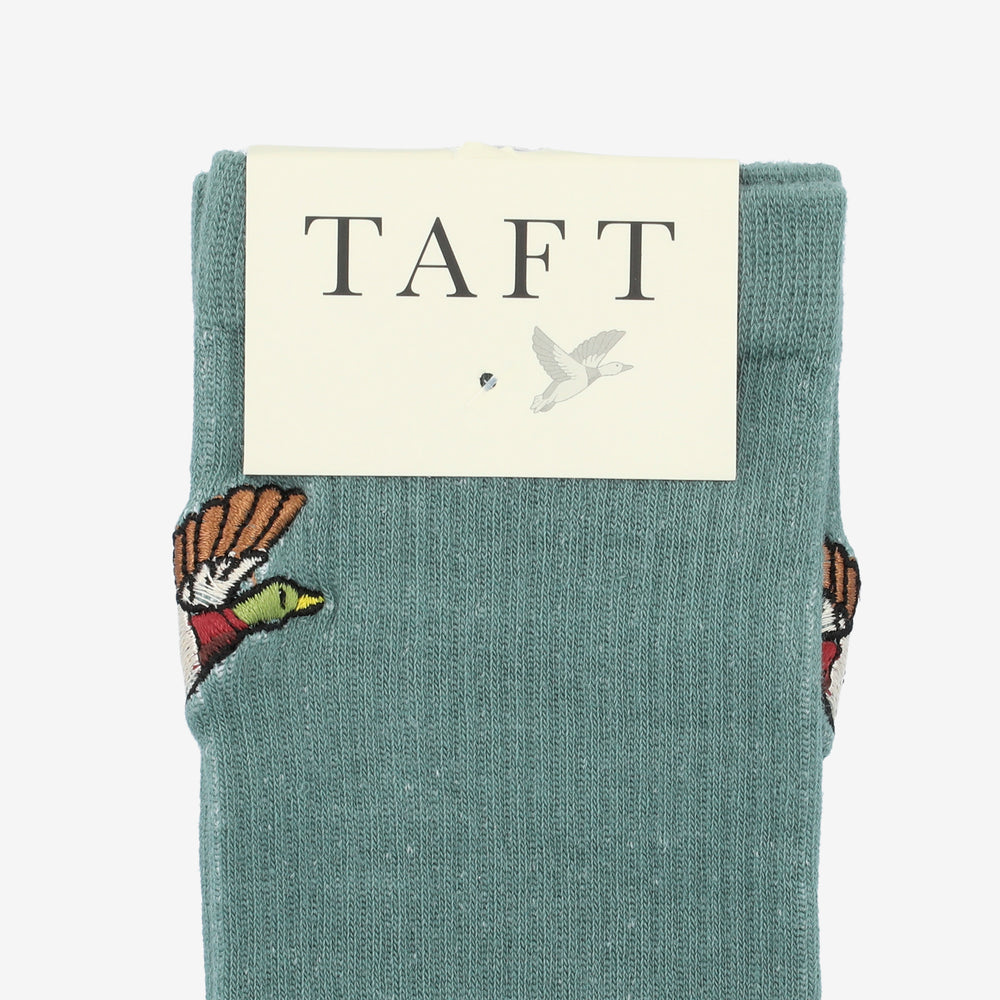 A pair of teal socks with an embroidered bird design near the top. The socks are displayed with a label that reads TAFT.