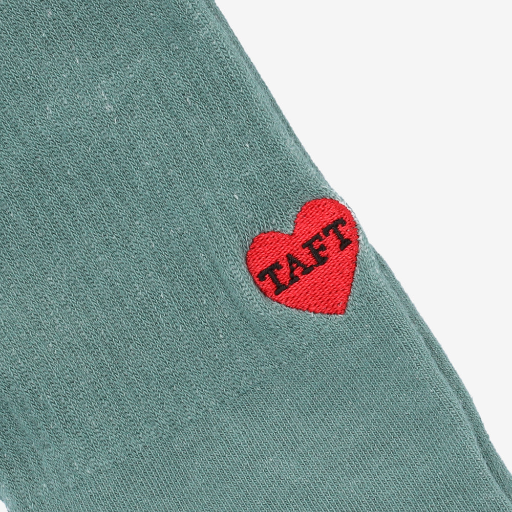 Close-up image of a green fabric with a red heart patch sewn on it, featuring the text TAFT.