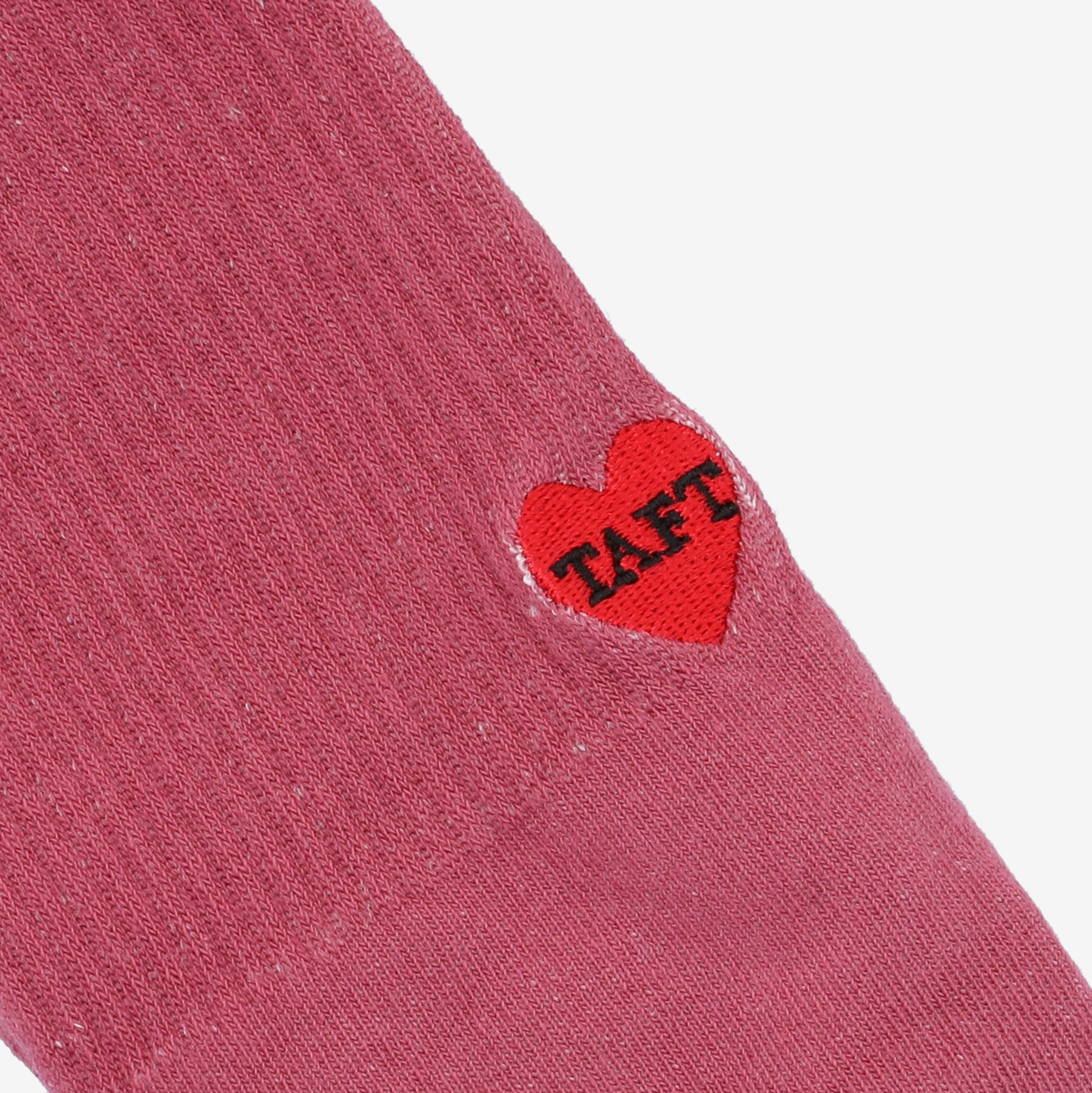 Close-up of a pink fabric with a red heart-shaped patch embroidered with the word TAFT in black letters.