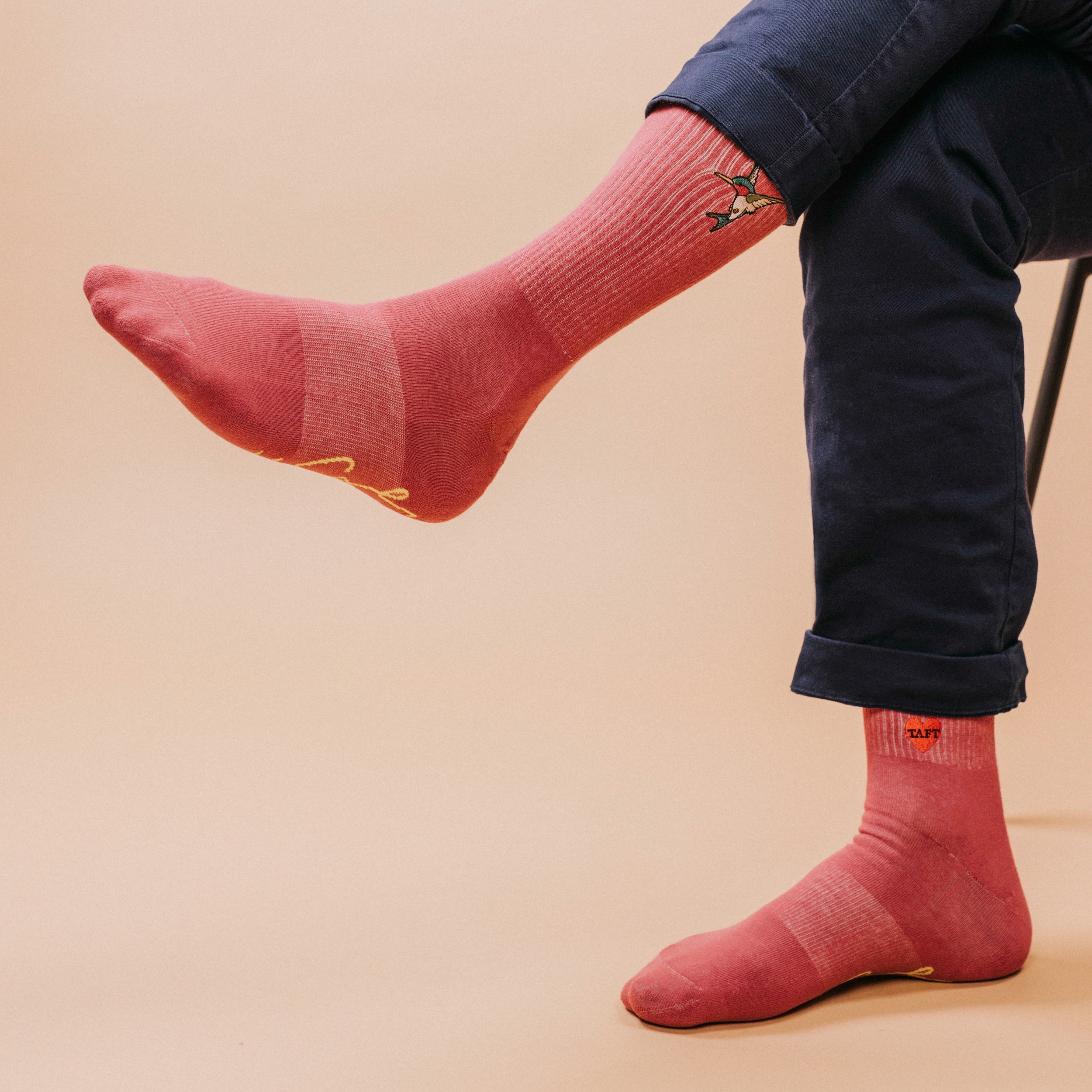 Person wearing pink socks with a design, seated on a chair, leg crossed over knee.