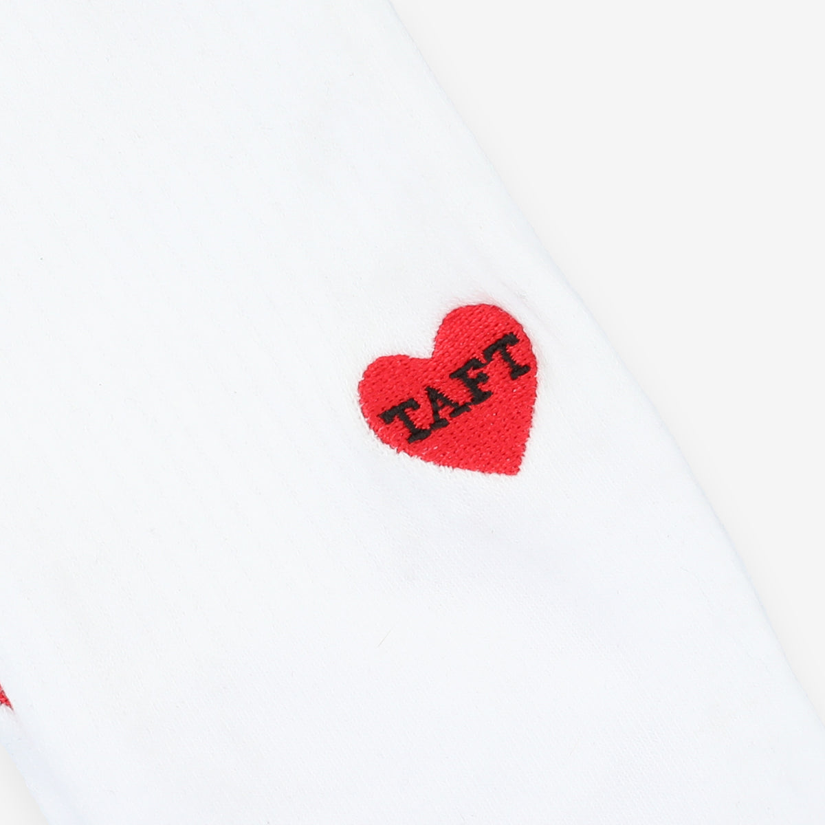 Close-up of a white fabric with a small red heart stitched with the word TAFT in black letters.