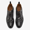 A pair of black leather shoes with intricate floral and bird patterns, featuring lace-up fronts and brown interiors.