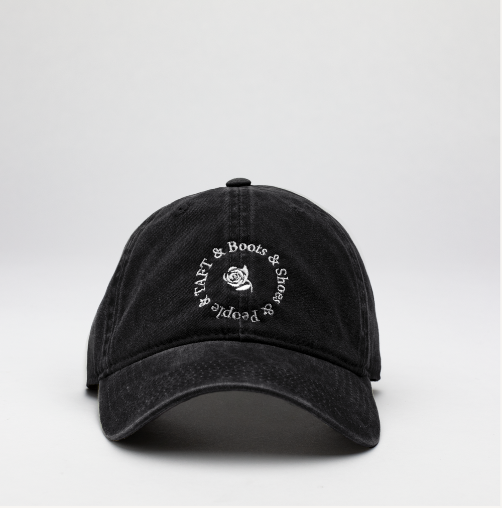 A black baseball cap with the text TAFT & Boots & Shoes People embroidered around a small white rose design on the front.