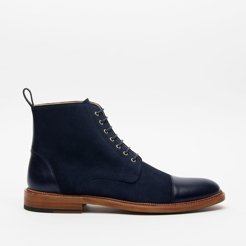 A side view of a navy blue leather and suede lace-up boot with a wooden sole against a plain white background.