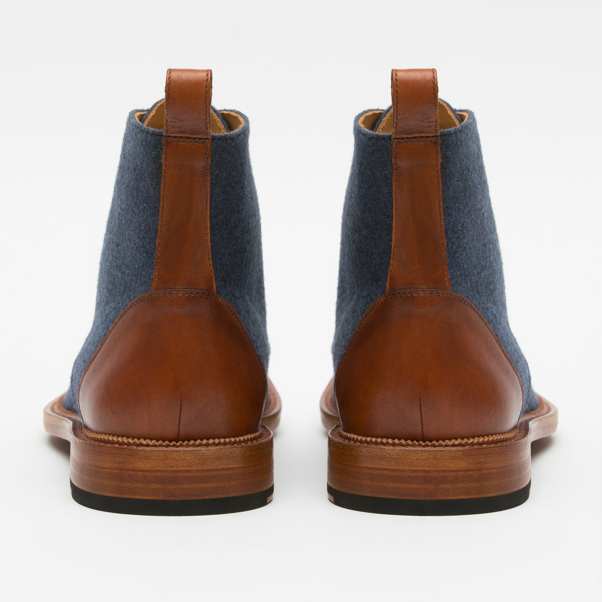 A pair of blue fabric boots with brown leather accents and pull tabs viewed from the back.