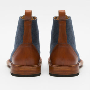 A pair of blue fabric boots with brown leather accents and pull tabs viewed from the back.