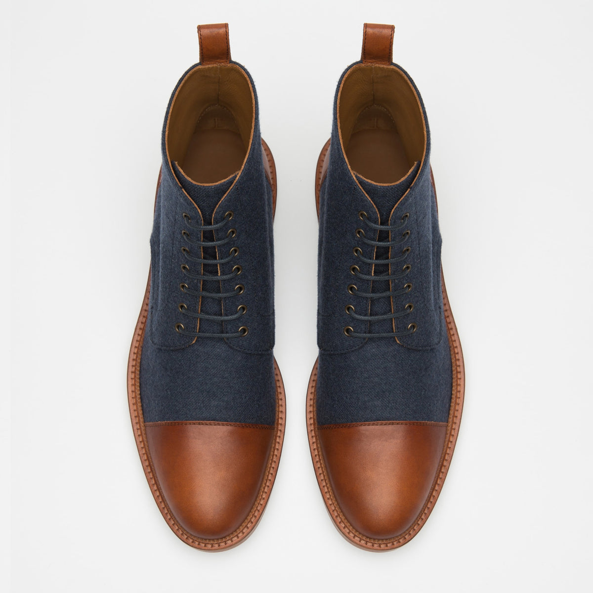 A pair of brown and navy lace-up ankle boots viewed from above, featuring brown leather toe caps, heel caps, and a brown leather trim, with navy fabric on the sides.