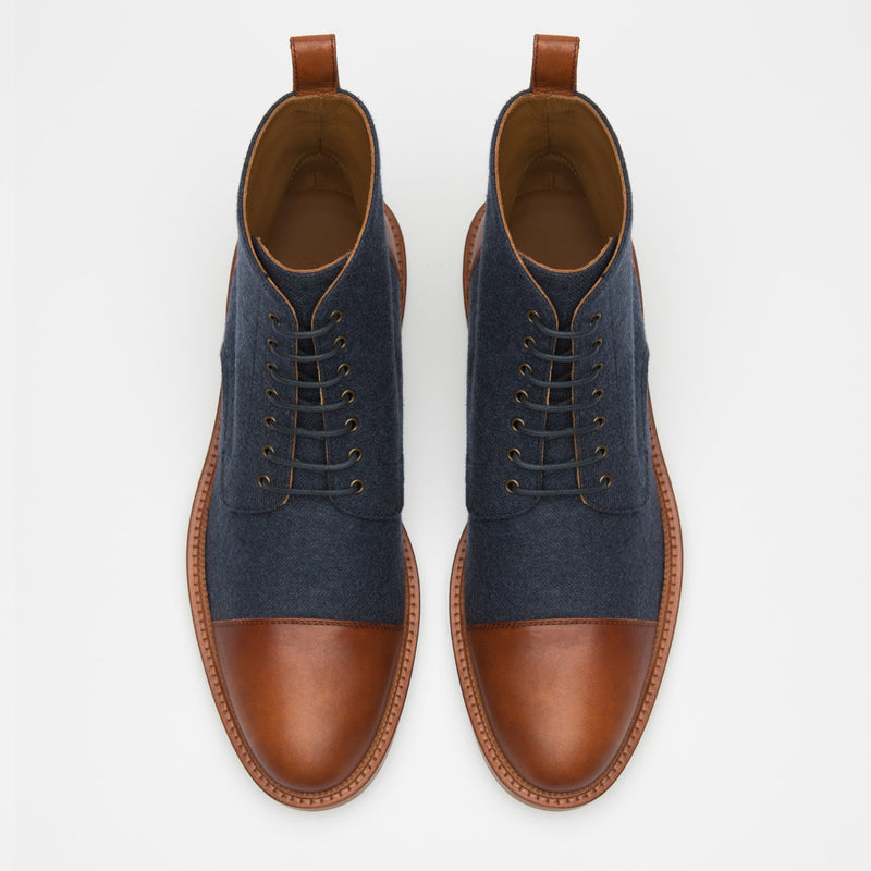 A pair of brown and navy lace-up ankle boots viewed from above, featuring brown leather toe caps, heel caps, and a brown leather trim, with navy fabric on the sides.