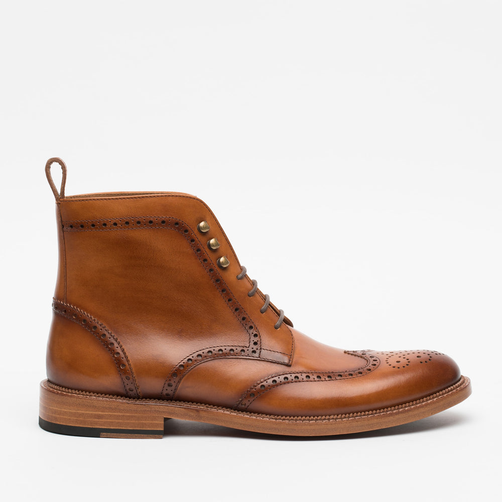 A tan leather brogue boot with decorative perforations, metal eyelets, laces, and a wooden sole, displayed on a white background.