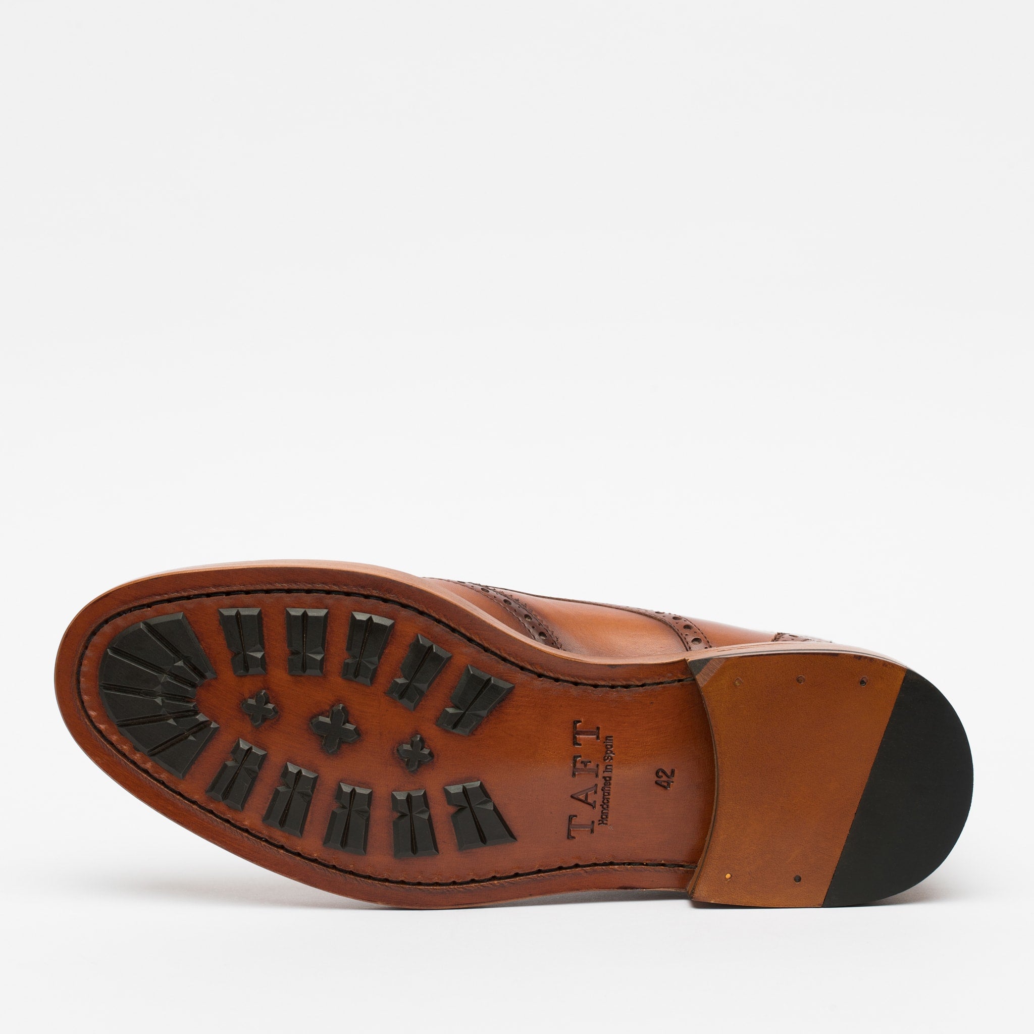 A brown leather shoe lying on its side, displaying the sole with black rubber treads and the brand name TAFT imprinted on it.