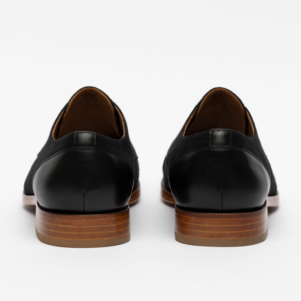 Rear view of a pair of black leather dress shoes with wooden soles on a white background.