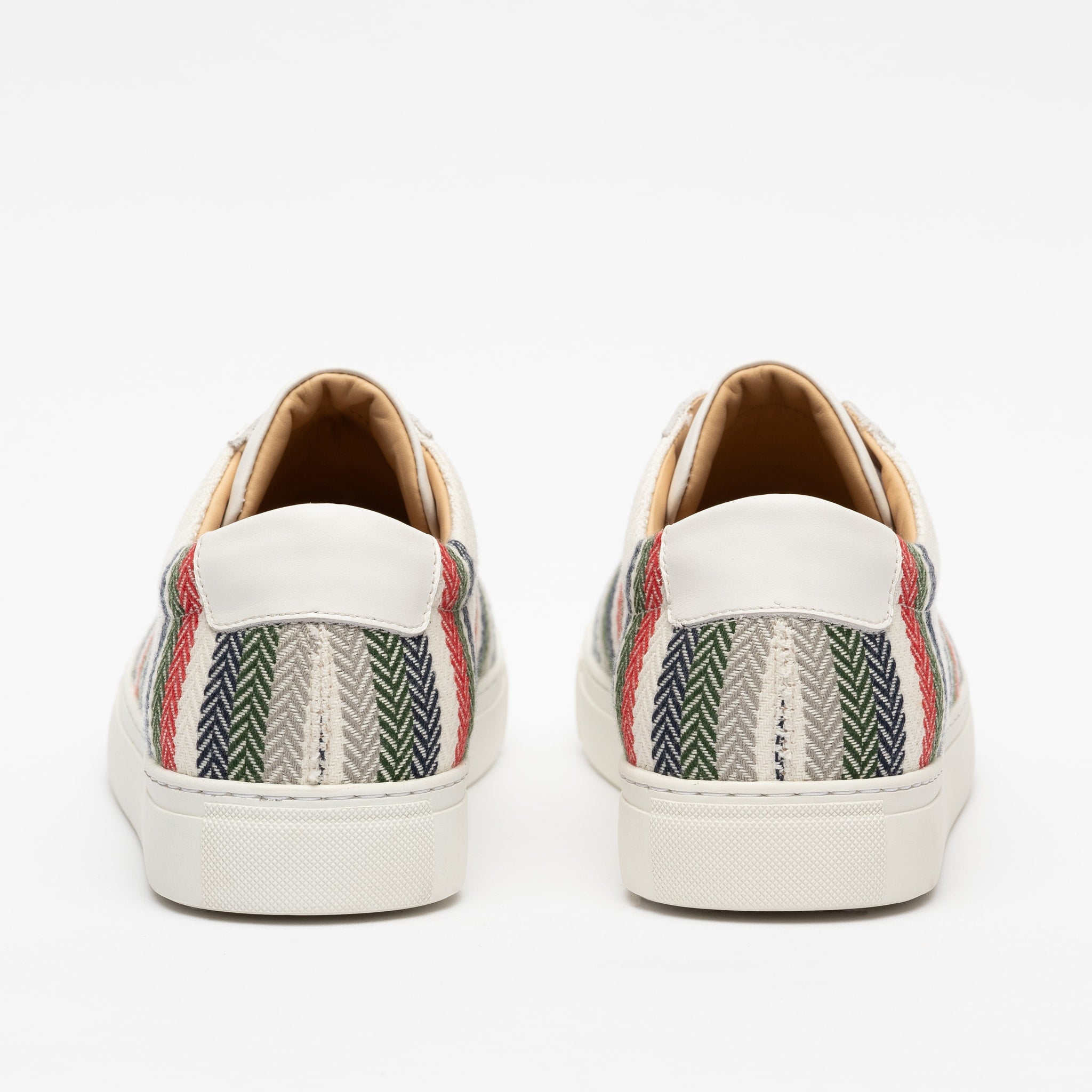 Back view of a pair of sneakers with a multicolored striped and herringbone pattern on the sides, white soles, and white heel sections.