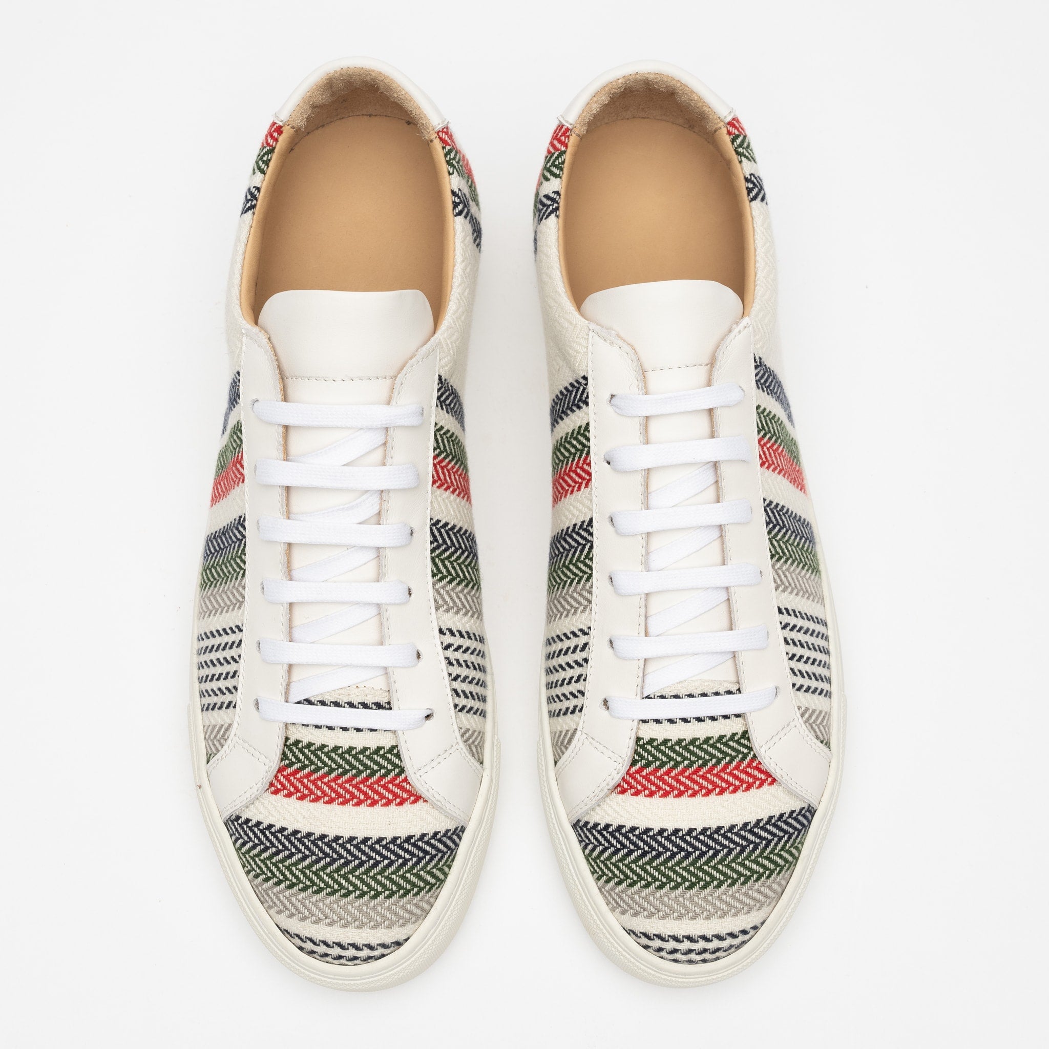 A pair of white sneakers with colorful, zigzag patterned fabric overlays on the sides, viewed from above.