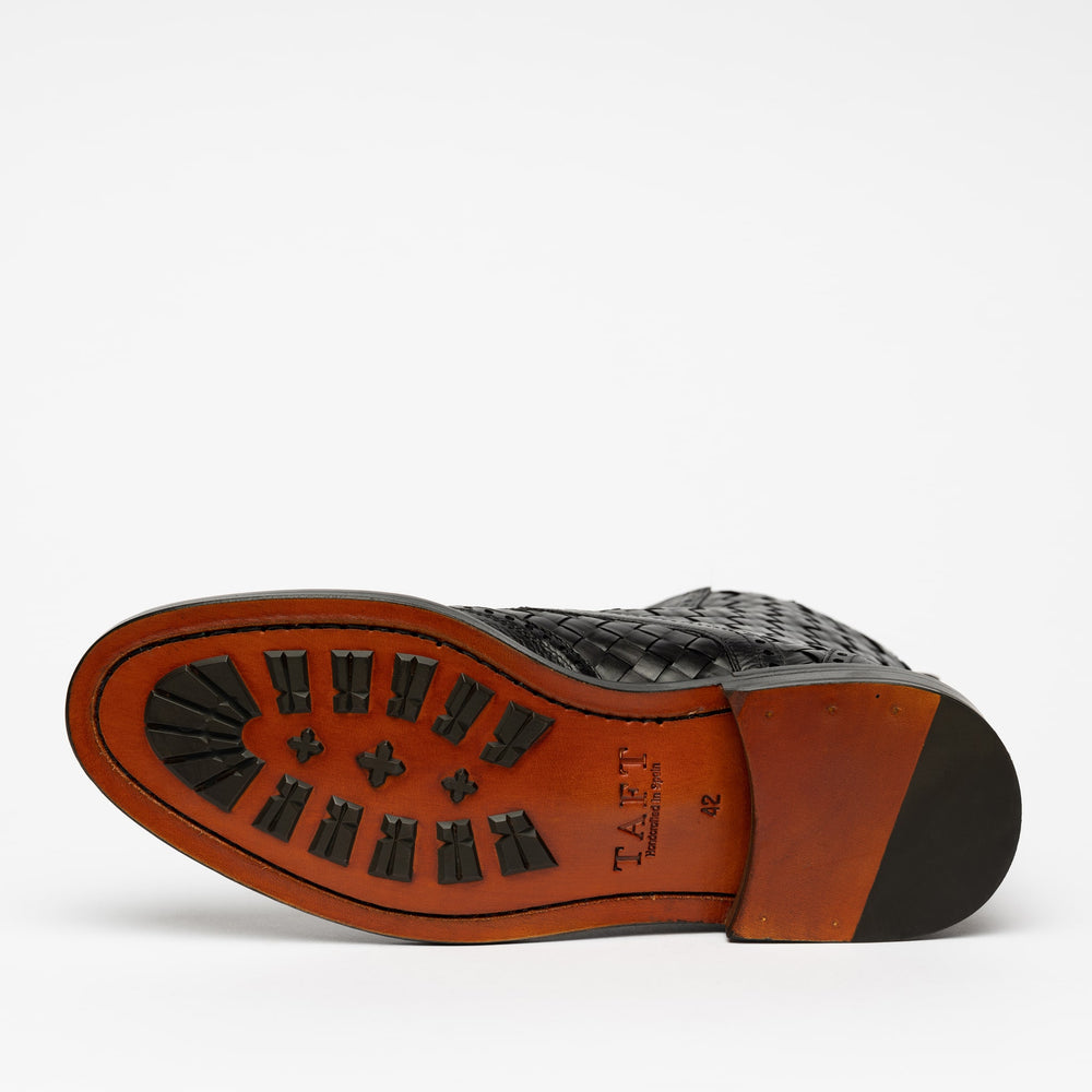 Close-up view of the sole of a black woven leather shoe, displaying tread pattern, wooden heel, and TAFT branding on the bottom.