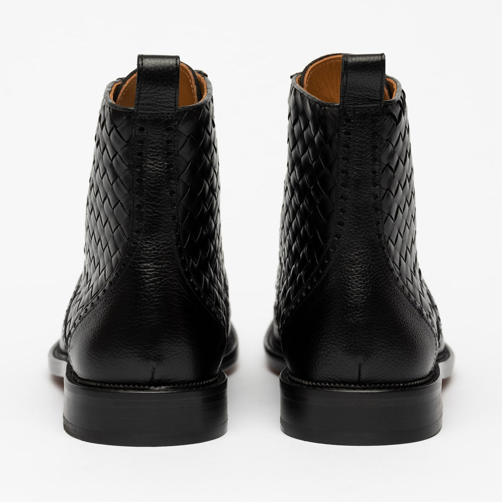 Back view of a pair of black leather boots with a braided design on the upper portion and smooth leather near the heel, against a white background.