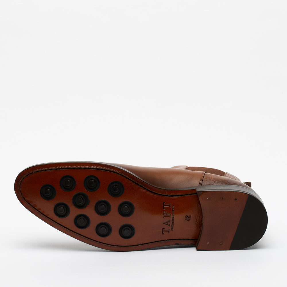 Bottom view of a brown leather dress shoe displaying a rubber-soled pattern with black circular grips and TAFT branding stamped on the sole.