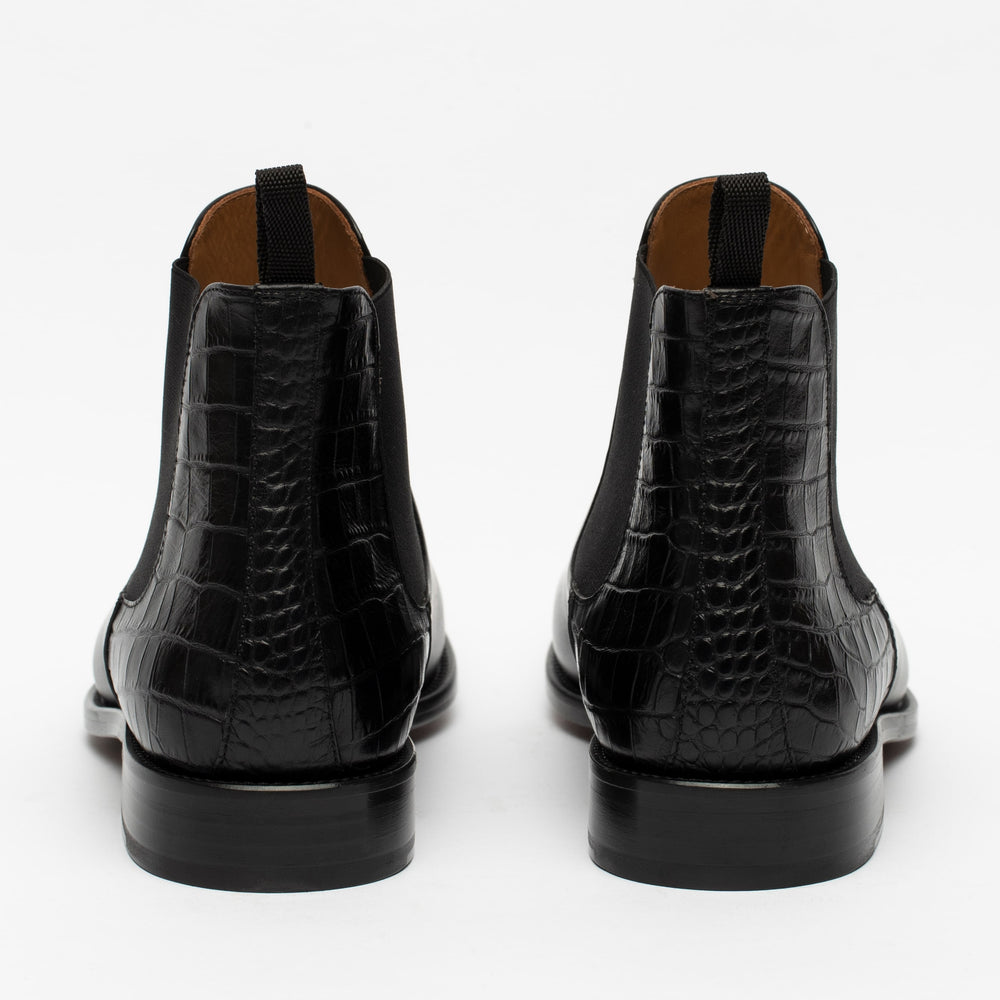 A pair of black leather ankle boots with a crocodile texture, shown from the back.