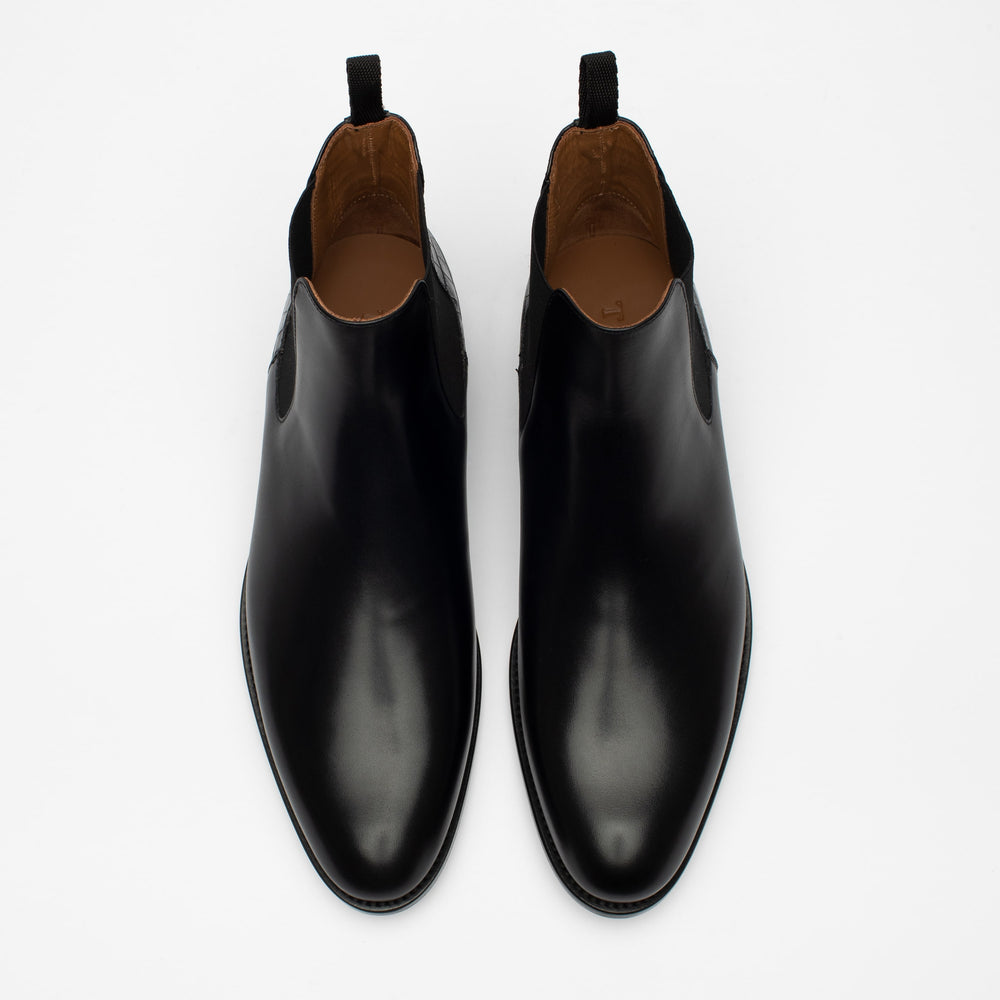 A pair of black leather slip-on shoes with black tabs at the heels, viewed from the top on a white background.