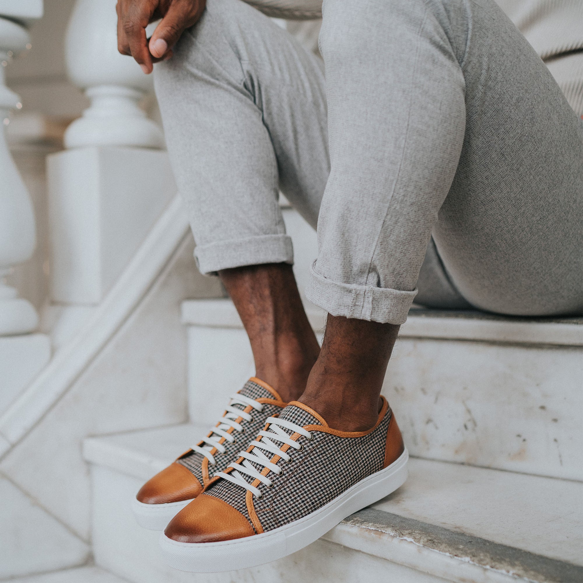 Jack Sneaker in Honey on Model sitting on white steps wearing grey cuffed pants