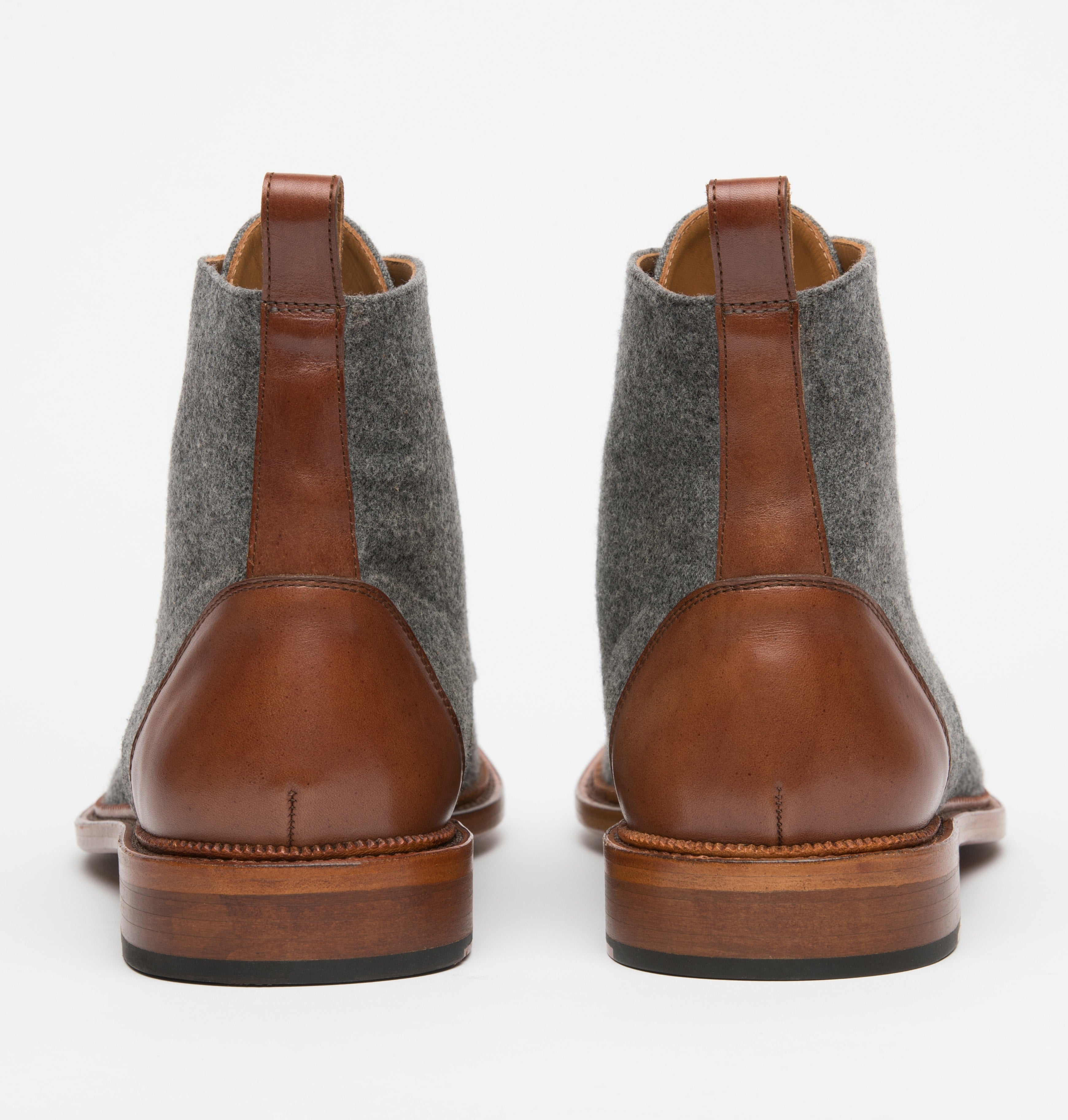 Rear view of a pair of brown leather and grey wool ankle boots with brown pull tabs, standing on a white background.