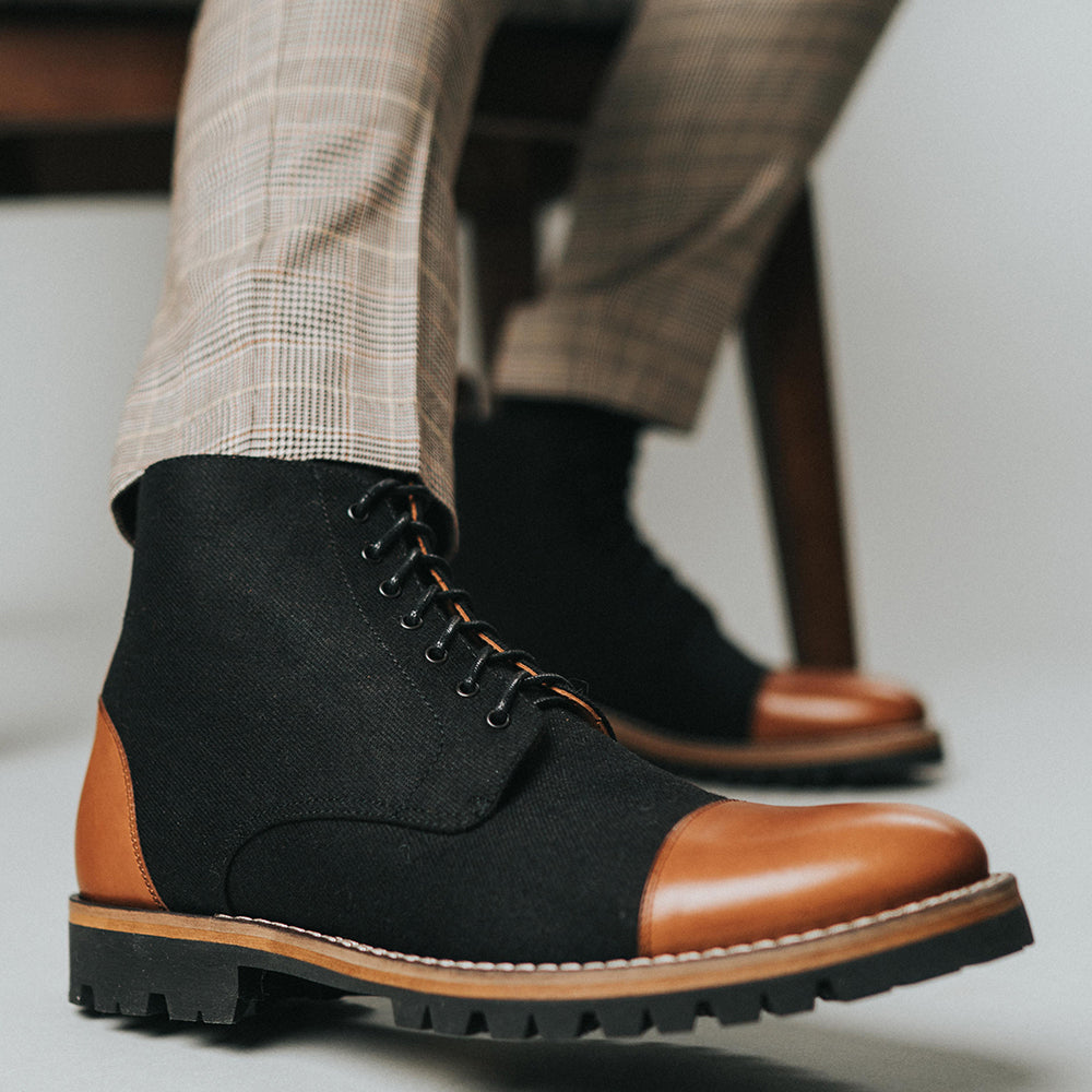 The Jack Boot in Industrial on model sitting in a wooden chair wearing plaid pants {{featured-B}}
