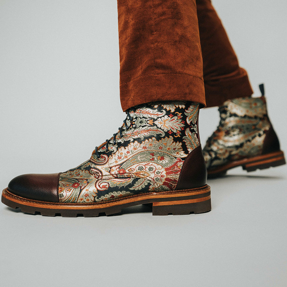 Person wearing brown suede pants and ornate paisley-patterned boots with brown leather accents and sturdy soles.