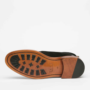 Bottom view of a black leather shoe with a brown sole and black rubber treads.
