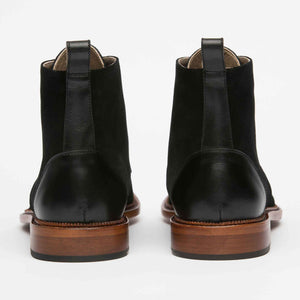 A pair of black leather boots with brown wooden soles, viewed from the back.